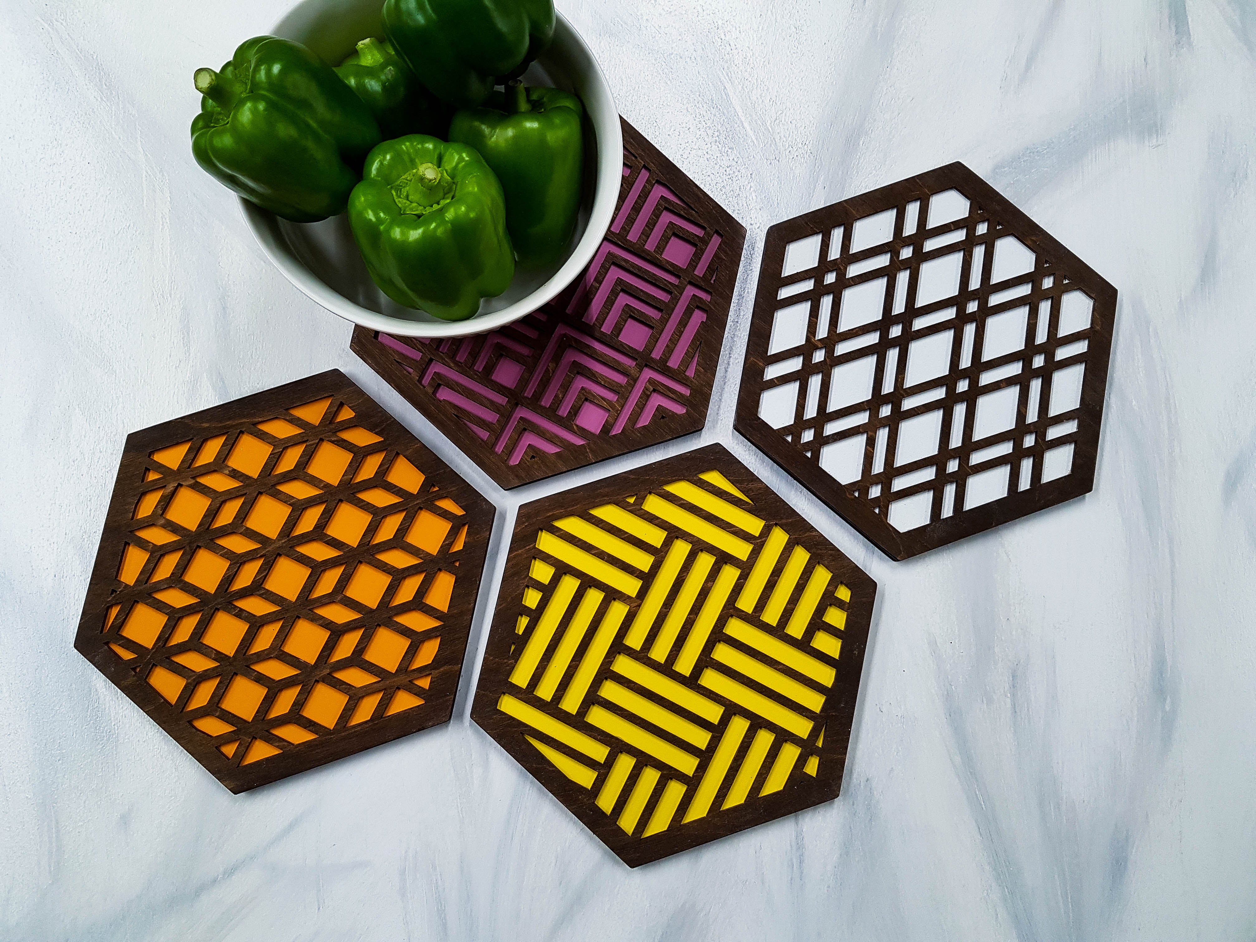 Example set of four mix-and-match walnut hexagon trivets arranged on a dining table. Shows how geometric slats, diamond, arrow, and square patterns look together in a complete mid-century modern table setting. Handmade in Ontario, Canada.